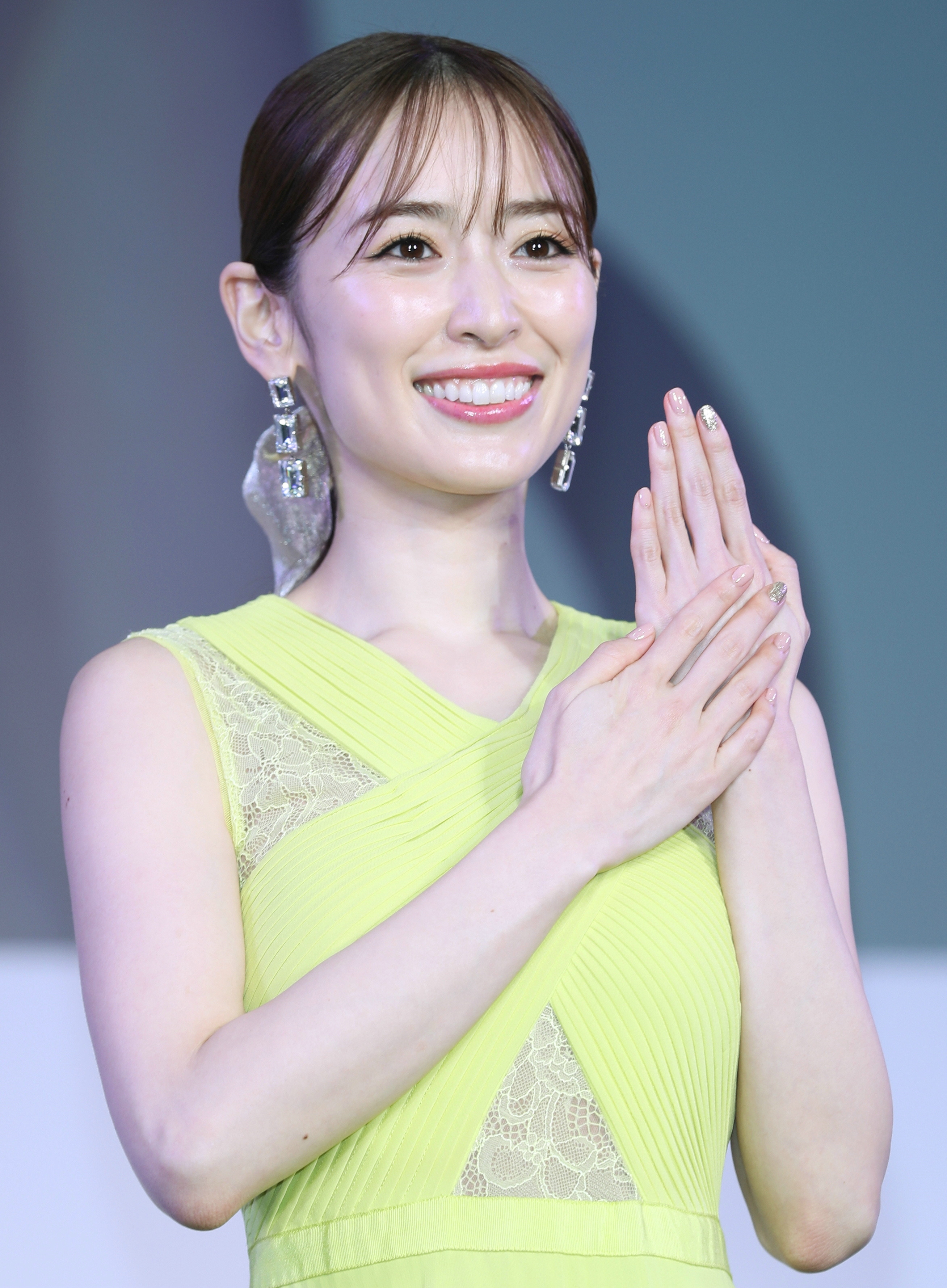 女性がノースリーブのドレスを着て微笑んでいます。ドレスにレースのディテールがあります。