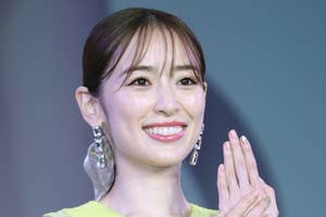 女性がノースリーブのドレスを着て微笑んでいます。ドレスにレースのディテールがあります。