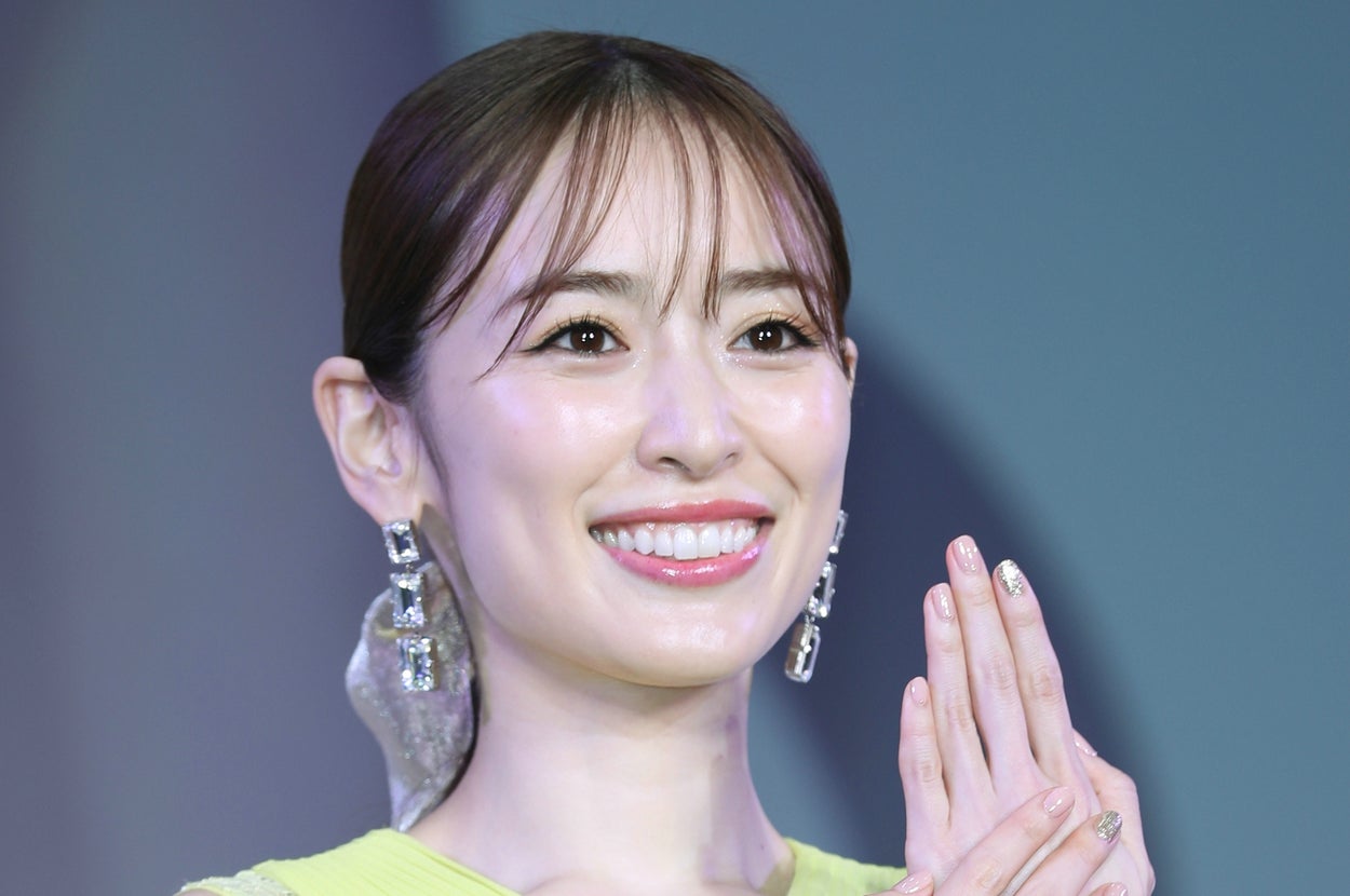 セレブ風の女性が笑顔で手を合わせ、レースのディテールがある華やかなドレスを着用しています。