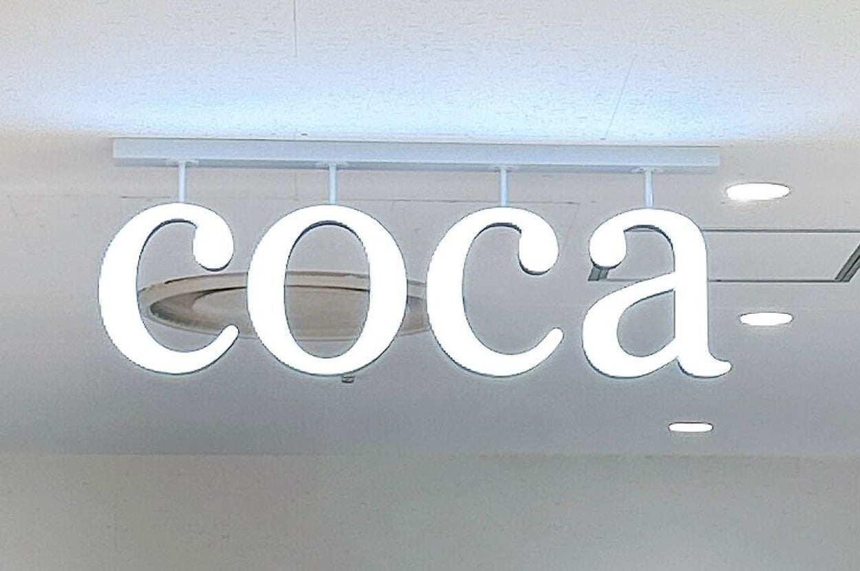 洋服店の天井にある「coca」というネオンサイン。背景には衣類が並んでいる。