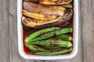 容器に入ったナスとオクラの料理。ナスはスライスされ、焼き色が付いています。オクラはそのまま置かれています。