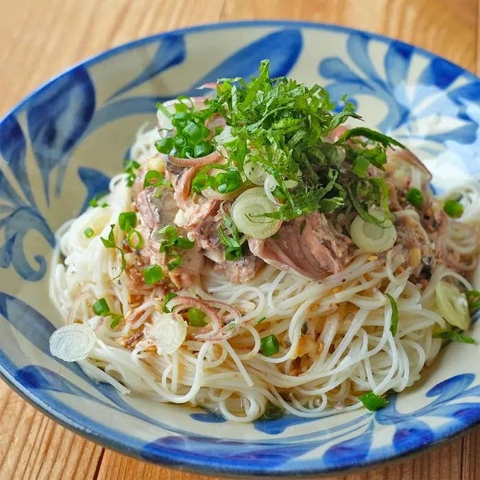 麺の上に細かく刻んだネギと香草がのせられた、美しく盛り付けられたそうめんの料理。