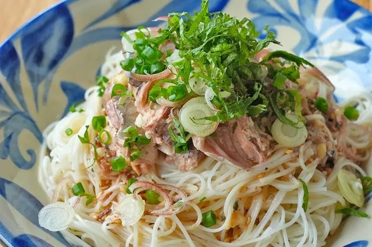 皿に盛られたそうめんの上に薬味や肉がのせられた冷たい麺料理。細かく刻んだネギとシソが添えられている。