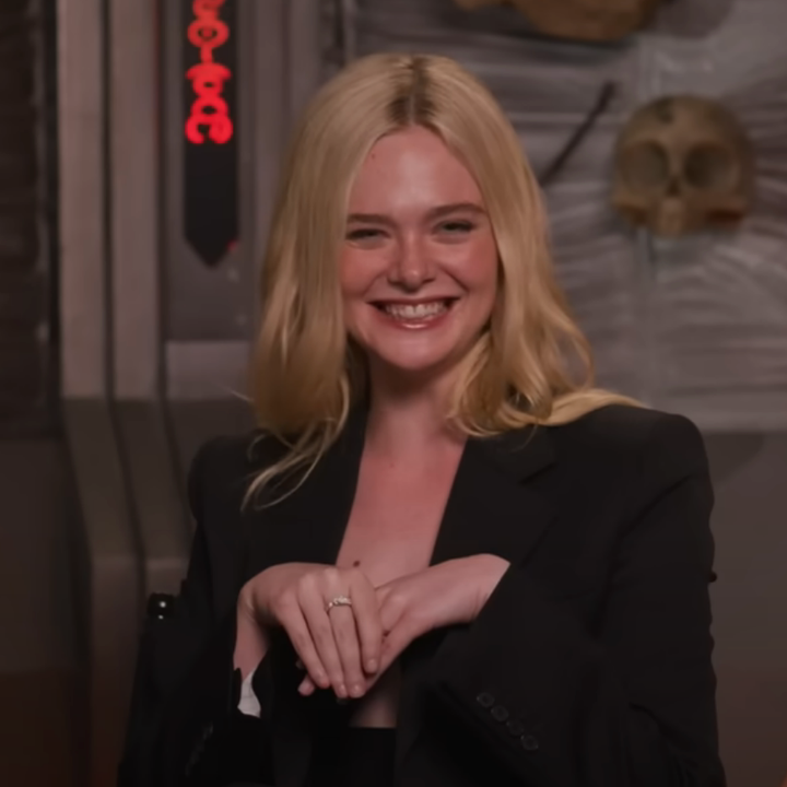 Person smiling, wearing a tailored black blazer, with hands playfully posed in a setting decorated with props