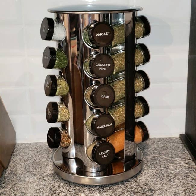 Rotating spice rack with labeled jars filled with various herbs and spices, such as parsley, basil, and celery salt, on a kitchen countertop