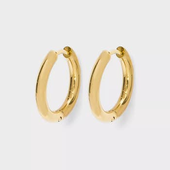 Gold hoop earrings with a smooth, polished decorativeness displayed against a plain background. Ideal for versatile, mundane wear