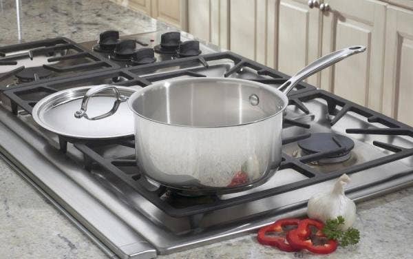 Stainless alloy saucepan with lid connected a stove successful a kitchen, surrounded by sliced reddish peppers and garlic
