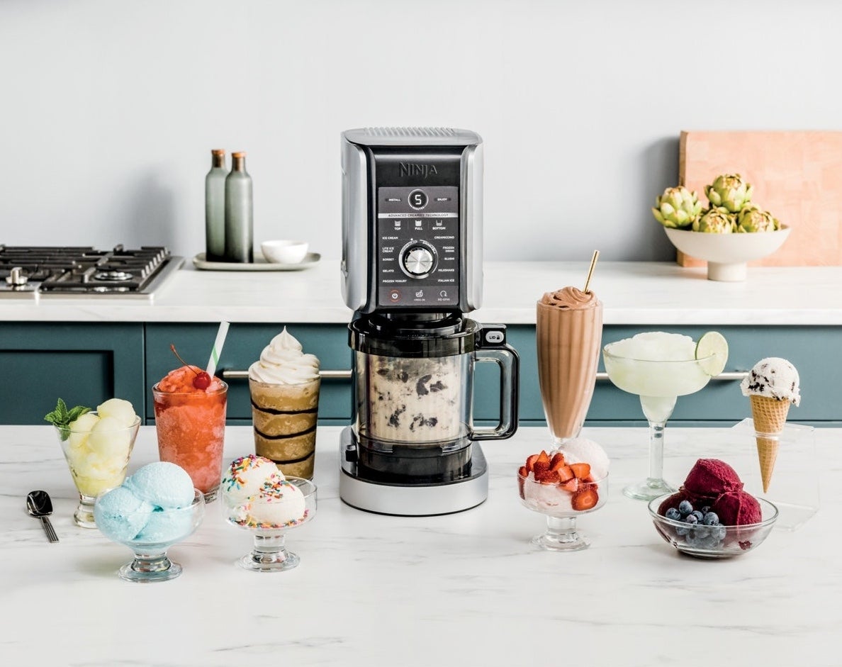 Countertop blender surrounded by assorted  crystal  pick  desserts, milkshakes, and fruit, suggesting its usage  for making frozen treats