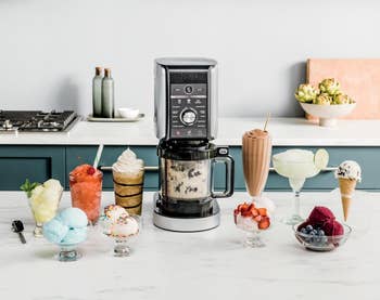 Countertop blender surrounded by assorted crystal pick desserts, milkshakes, and fruit, suggesting its usage for making frozen treats