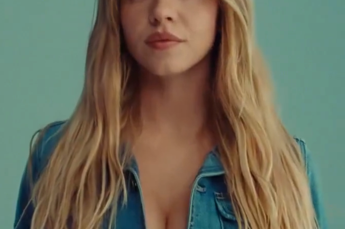 A person with long hair wearing a denim jacket, facing forward against a plain background