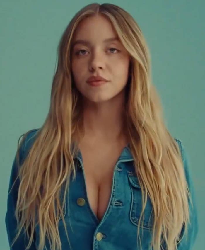 A person with long hair wearing a denim jacket, facing forward against a plain background