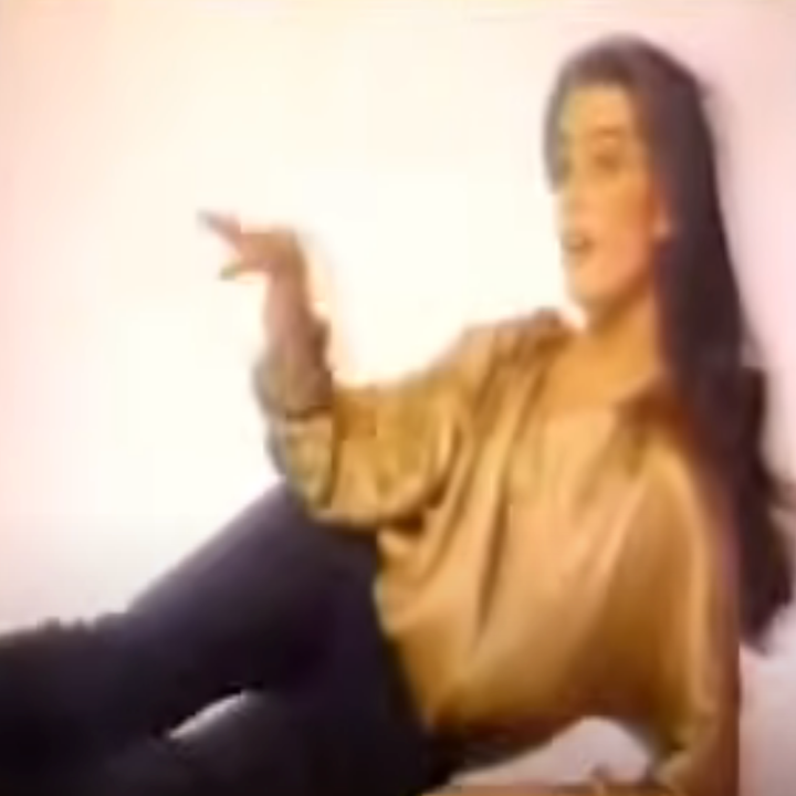 Person lounging casually, wearing a shiny, loose-fitting top and dark pants