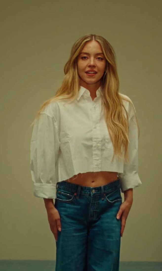 Person in casual attire with a white cropped shirt and jeans, standing against a plain background