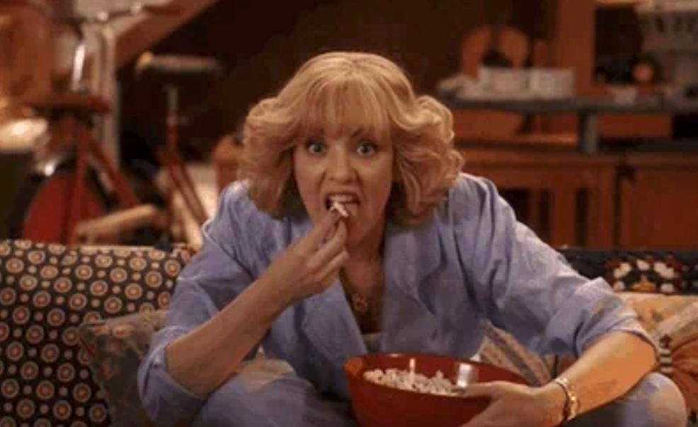 A person in a living room appears surprised, eating popcorn while watching TV, suggesting a scene related to work or financial news unfolding