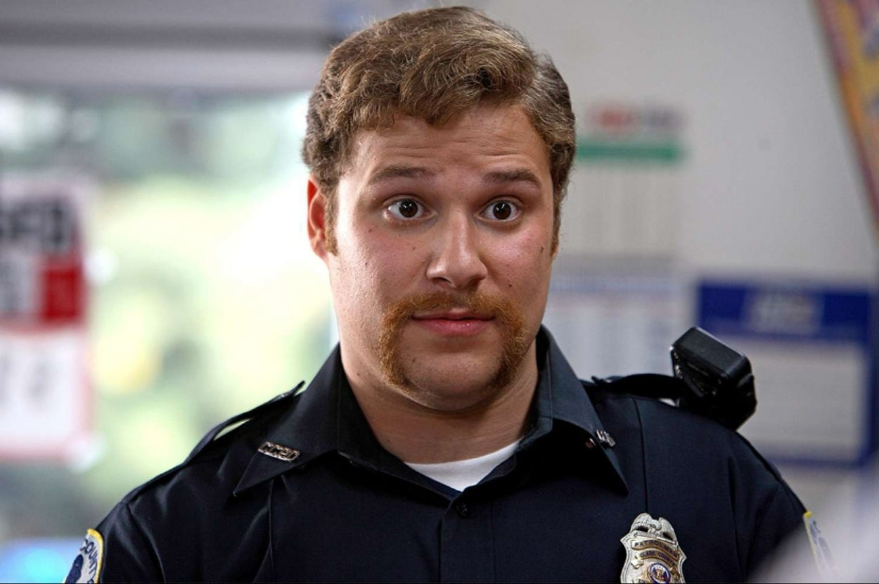 A person in a police uniform with a mustache looks directly at the camera, appearing curious or surprised