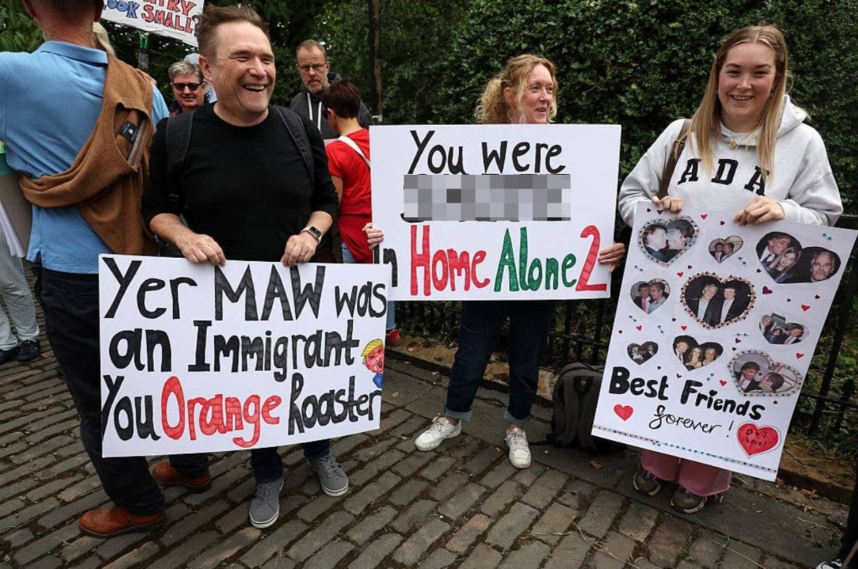Three people hold humorous protest signs referencing a celebrity's film roles and background, using wordplay and playful jabs