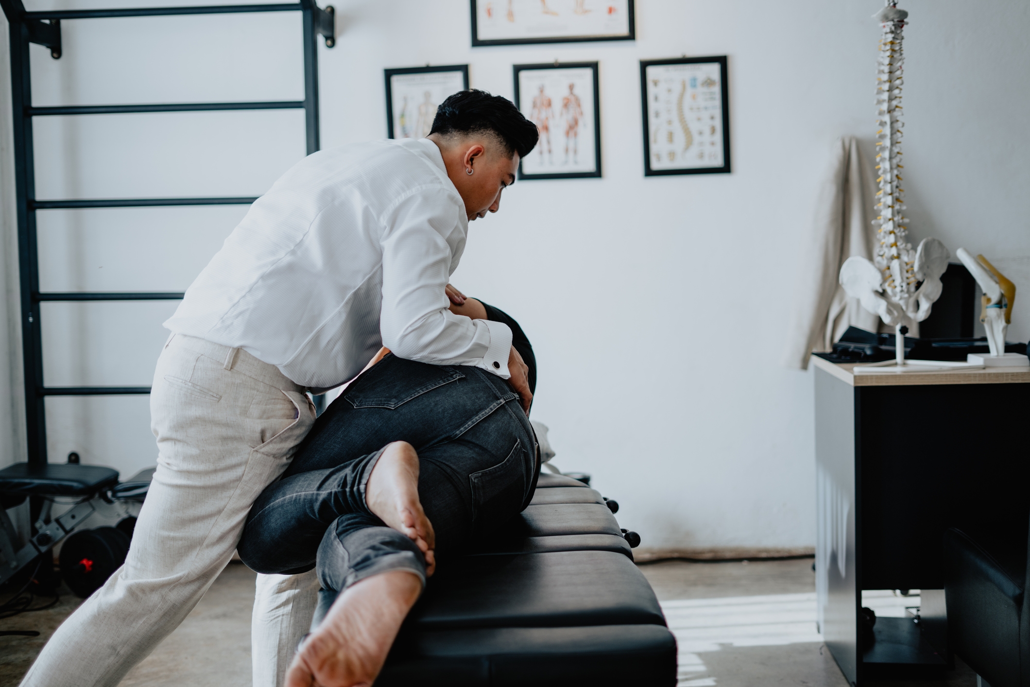 Person som mottar kiropraktisk justering på et behandlingsbord, omgitt av anatomiske plakater i en klinikkinnstilling