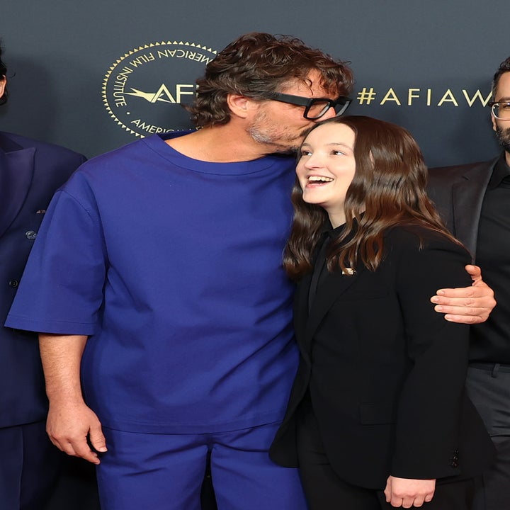 Two people on a red carpet, one in a casual loose-fitting outfit, the other in a neatly tailored suit, sharing a joyful moment