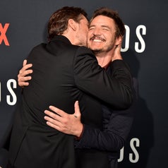 Two men joyfully embrace at a Netflix event. They are both in formal suits, radiating happiness on the red carpet