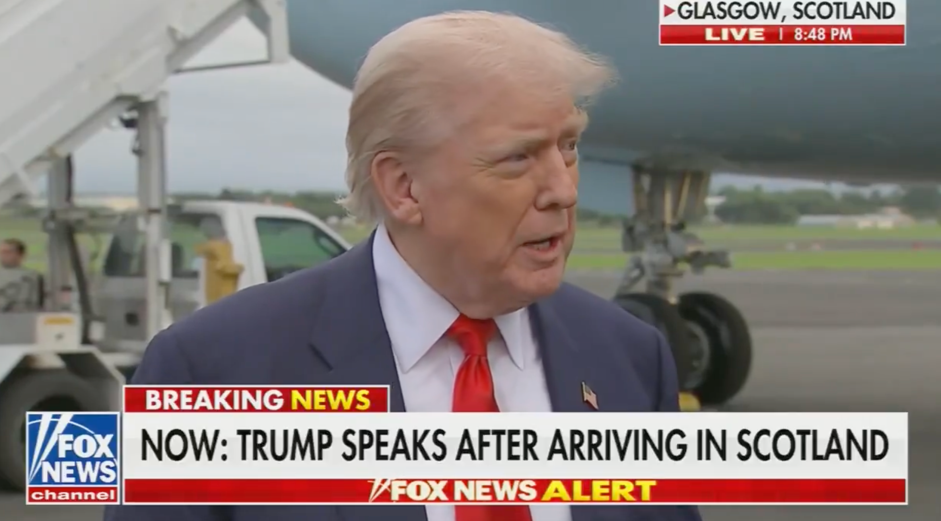 Man speaking to reporters after arriving in Scotland, near an airplane. News banner reads: &quot;Breaking News: Trump speaks after arriving in Scotland.&quot;