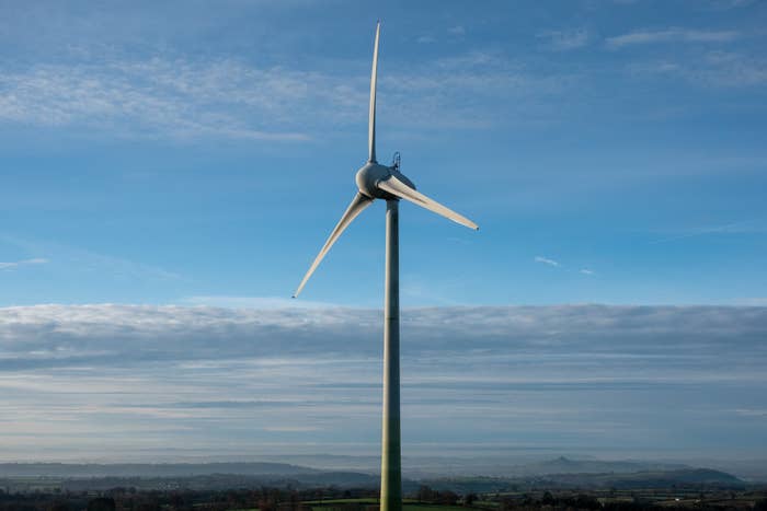 A single wind turbine stands tall against a backdrop of a cloudy sky and distant landscape, symbolizing renewable energy