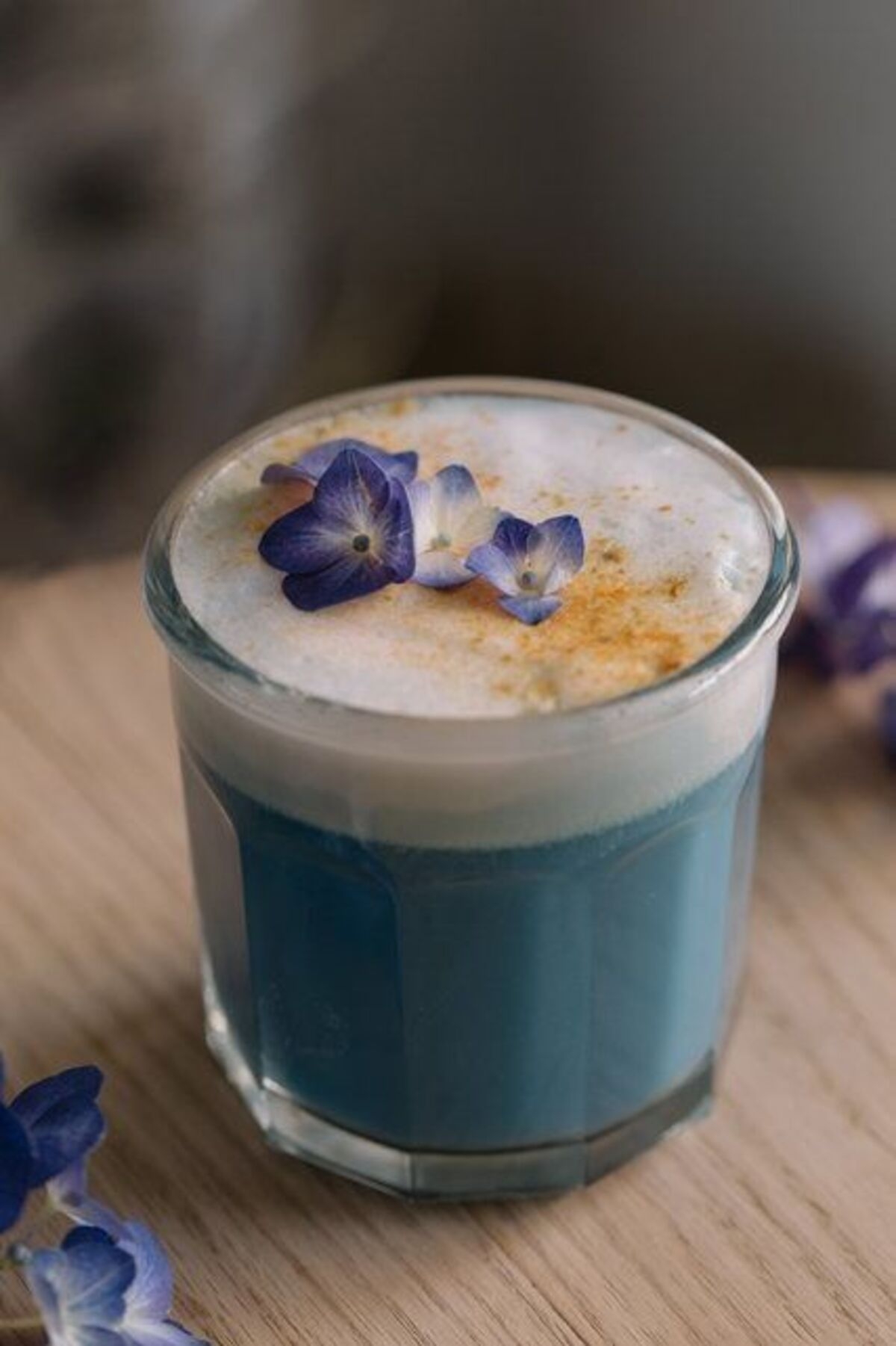Bebida con espuma blanca y flores pequeñas en la parte superior, servida en un vaso de vidrio sobre una mesa