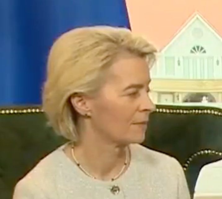 A person with short blond hair wearing a light top is sitting and looking to the side in an indoor setting