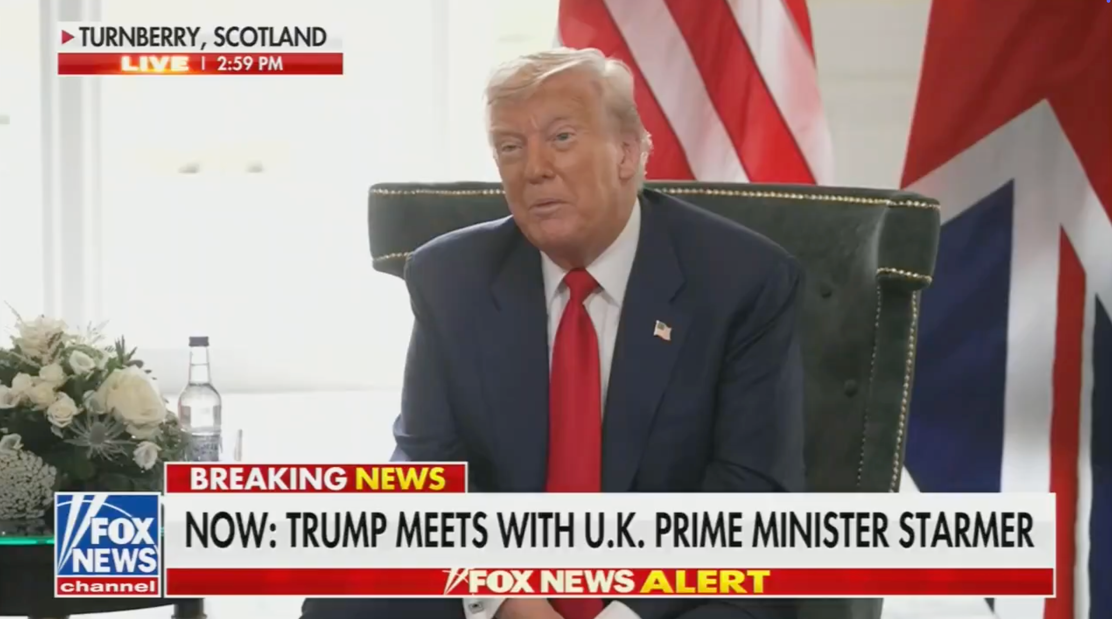 Person in suit sitting in a chair with Scottish and Union Jack flags in the background, watching TV news reporting on a meeting with U.K. Prime Minister Starmer