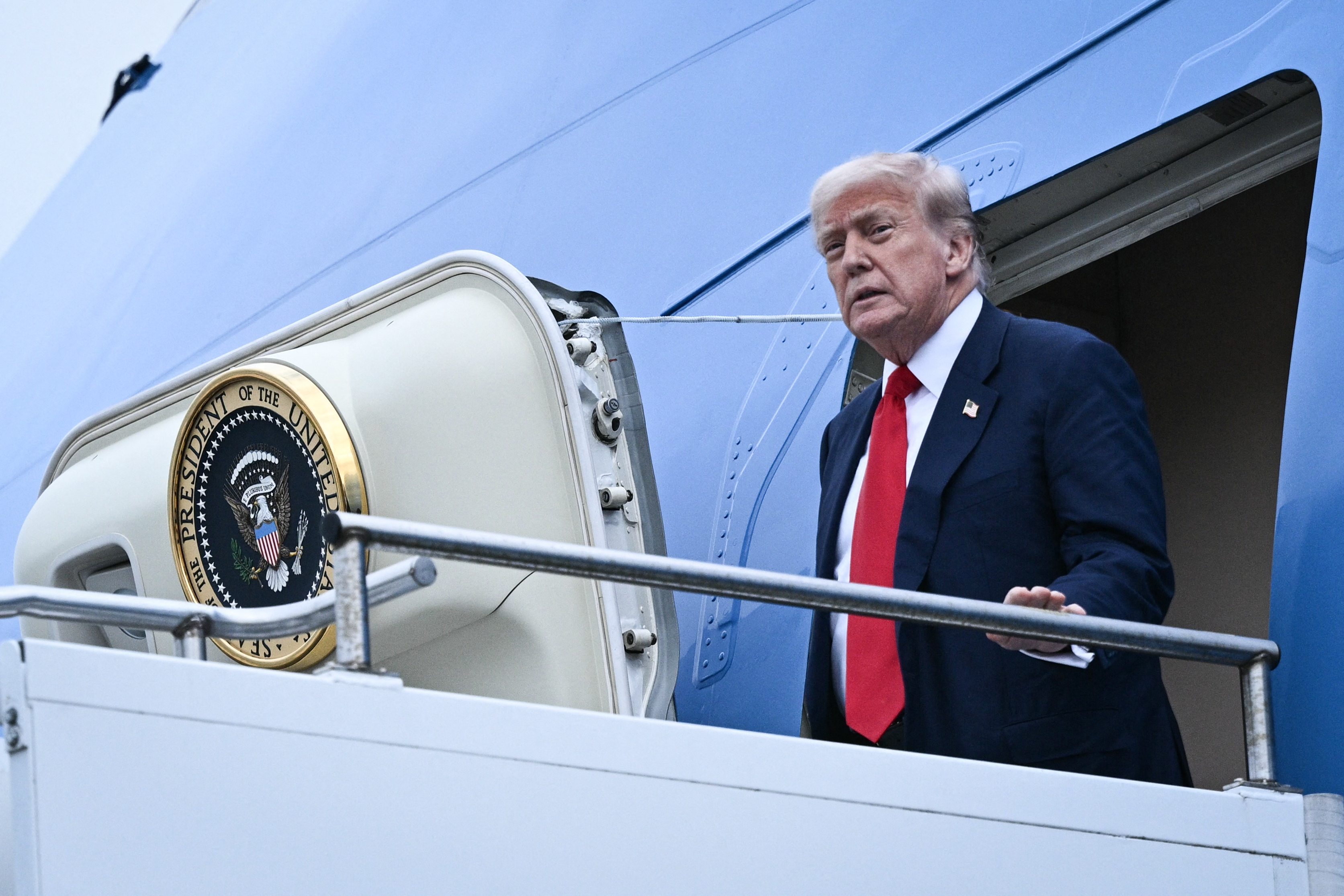 A person in a suit exits an airplane with a presidential seal by the door, suggesting a formal event or political context