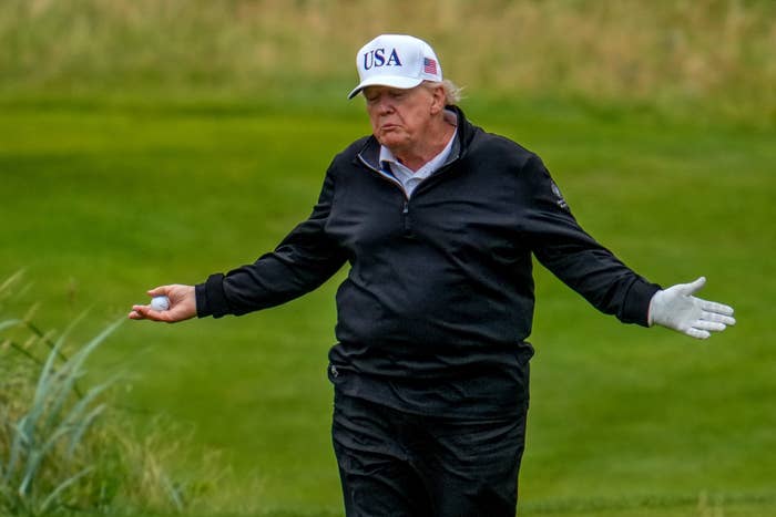 Person golfing, wearing a hat with "USA," a zip-up jacket, and gloves, holding a golf ball with an open-arm gesture on a grassy course