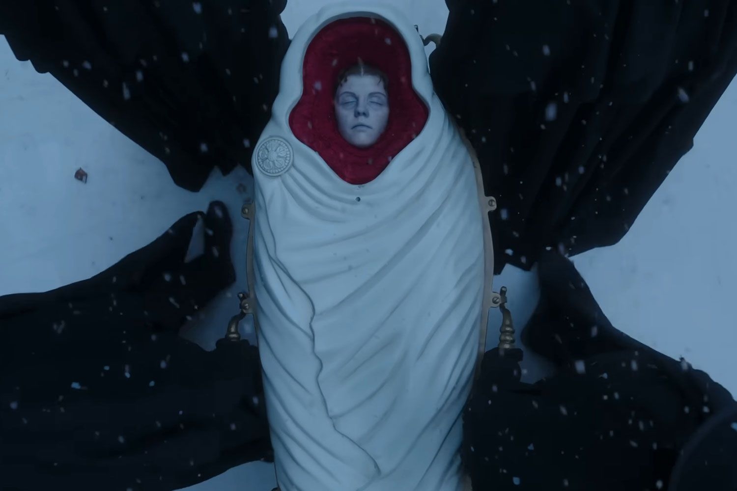 Imagen de una persona acostada, envuelta en un sudario con la cara descubierta, en un escenario invernal con nieve