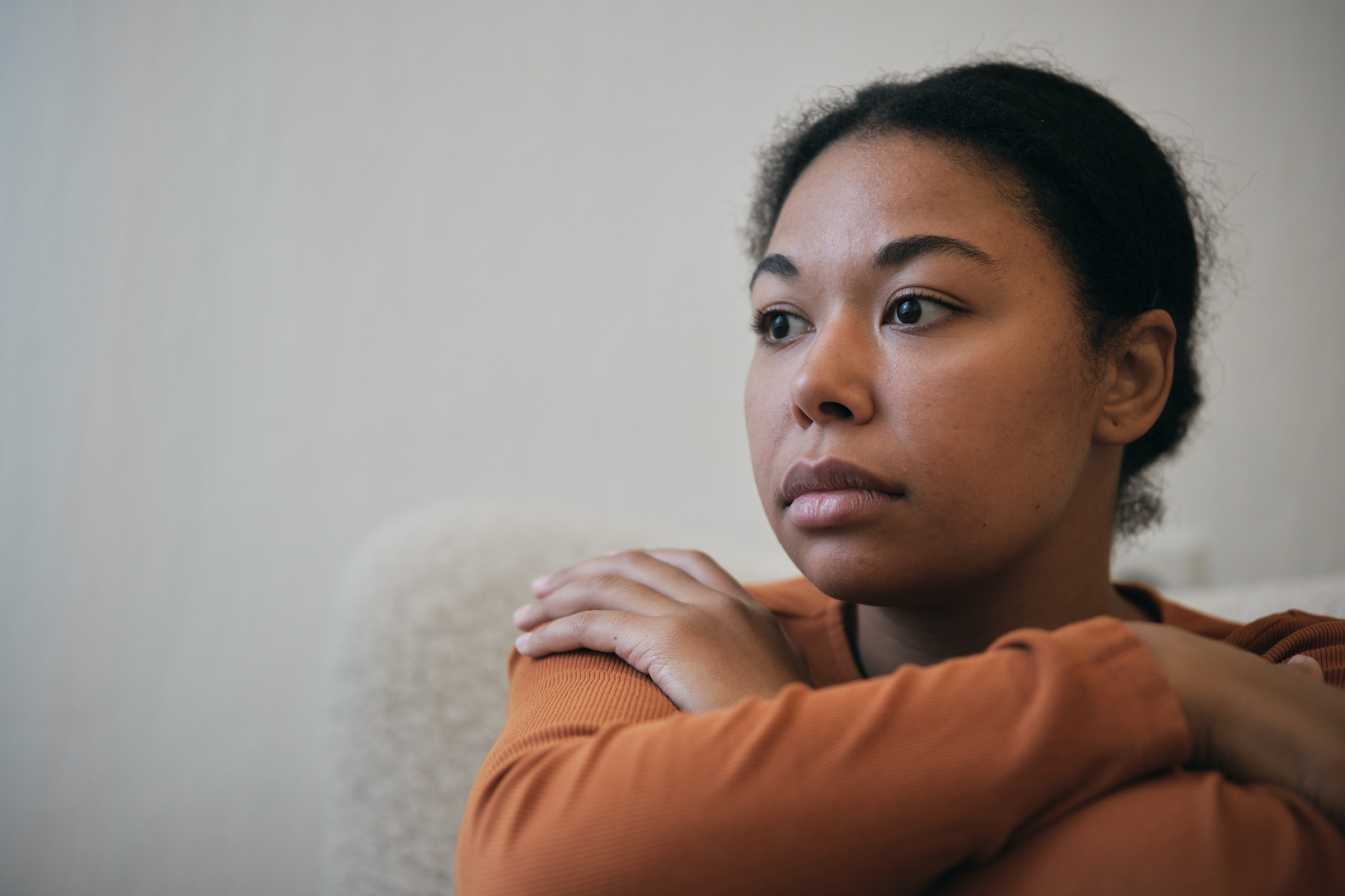 Person sittende, stirrer ettertenksomt til siden, armene hviler på knærne. Virker rolig og reflekterende, iført en langermet topp