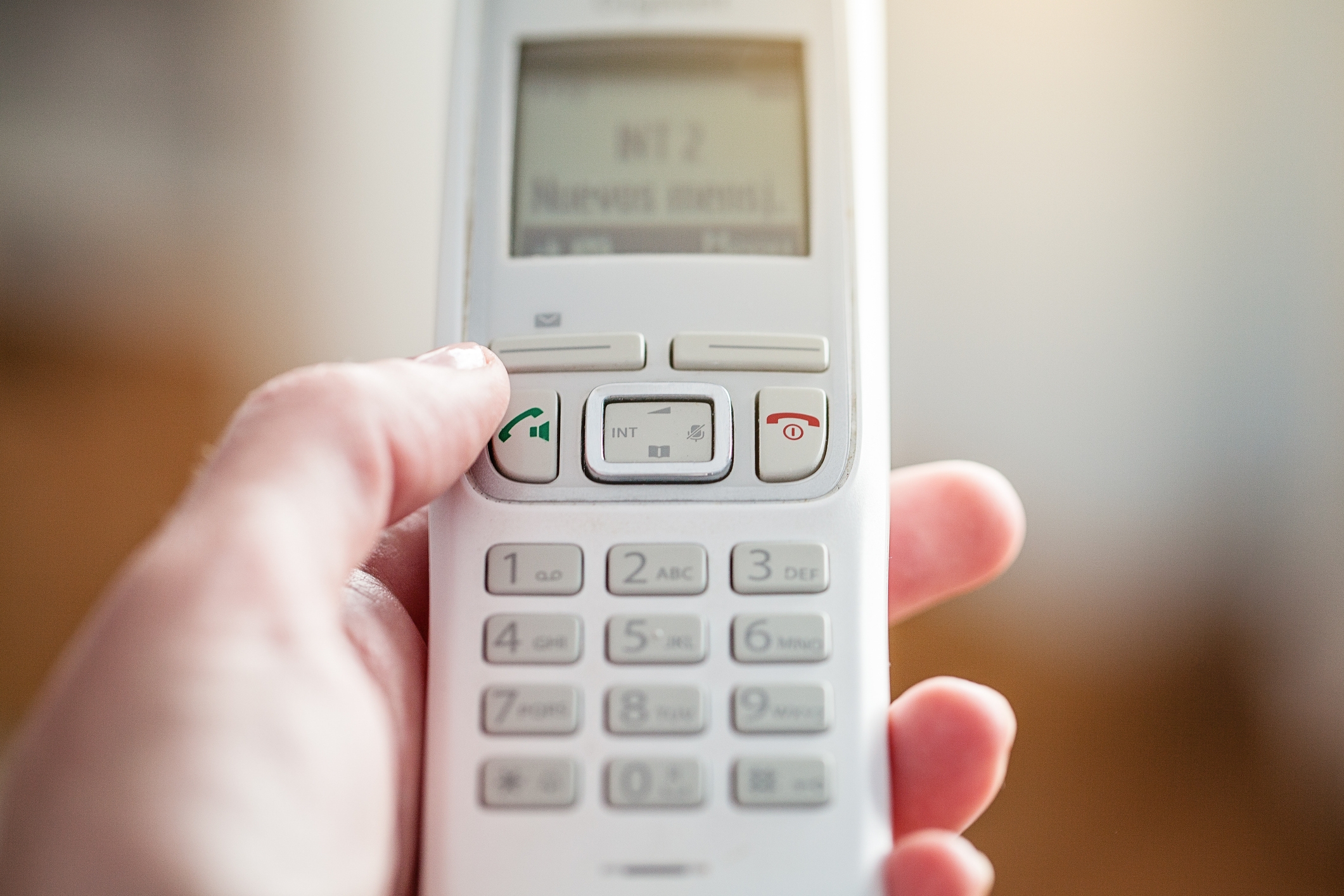 Hand holding a landline phone with a screen displaying blurred text, possibly dialing or navigating the menu options