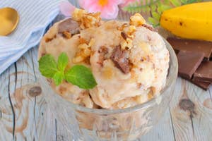 アイスクリームのデザートがクリスタルボウルに盛られ、チョコレートとナッツで飾られている。机の上にバナナが置かれている。