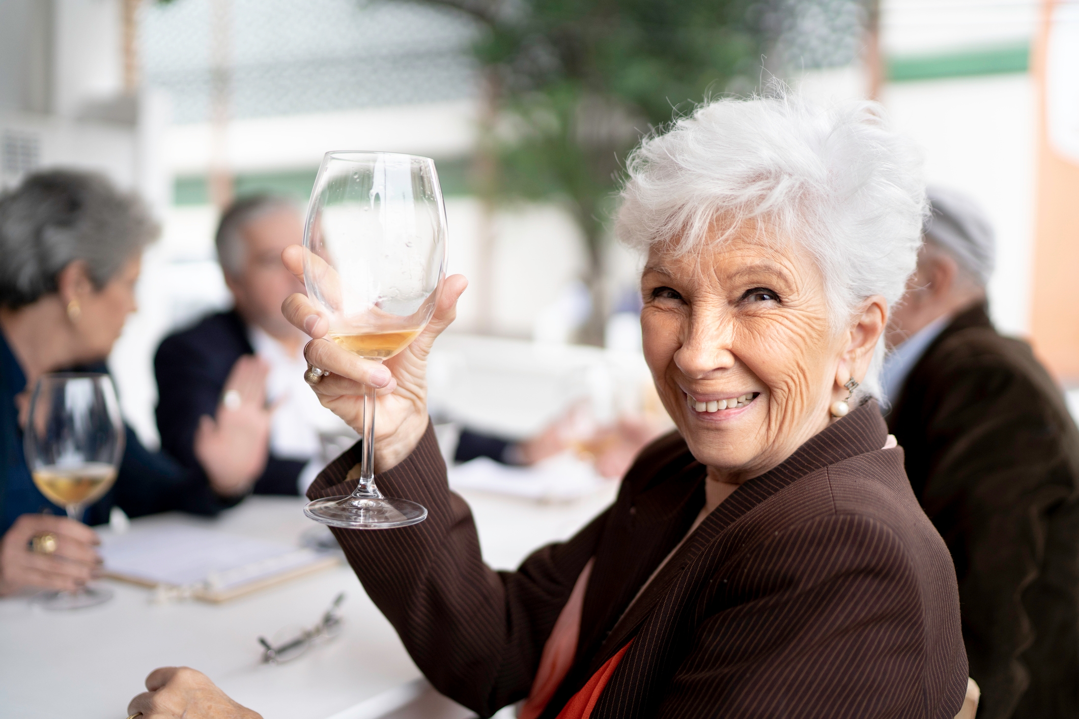 Eldre kvinne som smiler og oppdrar et vinglass i en toast på en utendørs sammenkomst med venner
