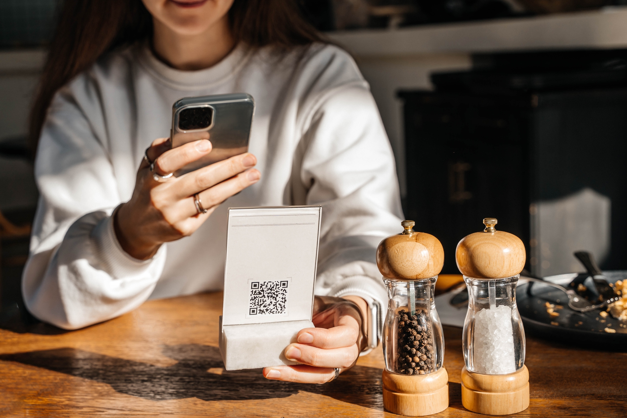 A person scans a QR code on a menu holder at a wooden table with a smartphone, next to salt and pepper shakers