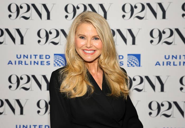 Person with long hair wearing a classic black outfit, smiling, at an event with "92NY" and "United Airlines" logos in the background