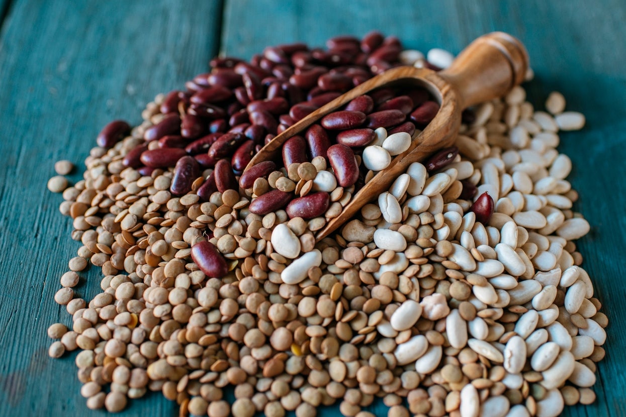 A wooden scoop on a pile of mixed legumes, including red and white beans, and lentils, on a wooden surface