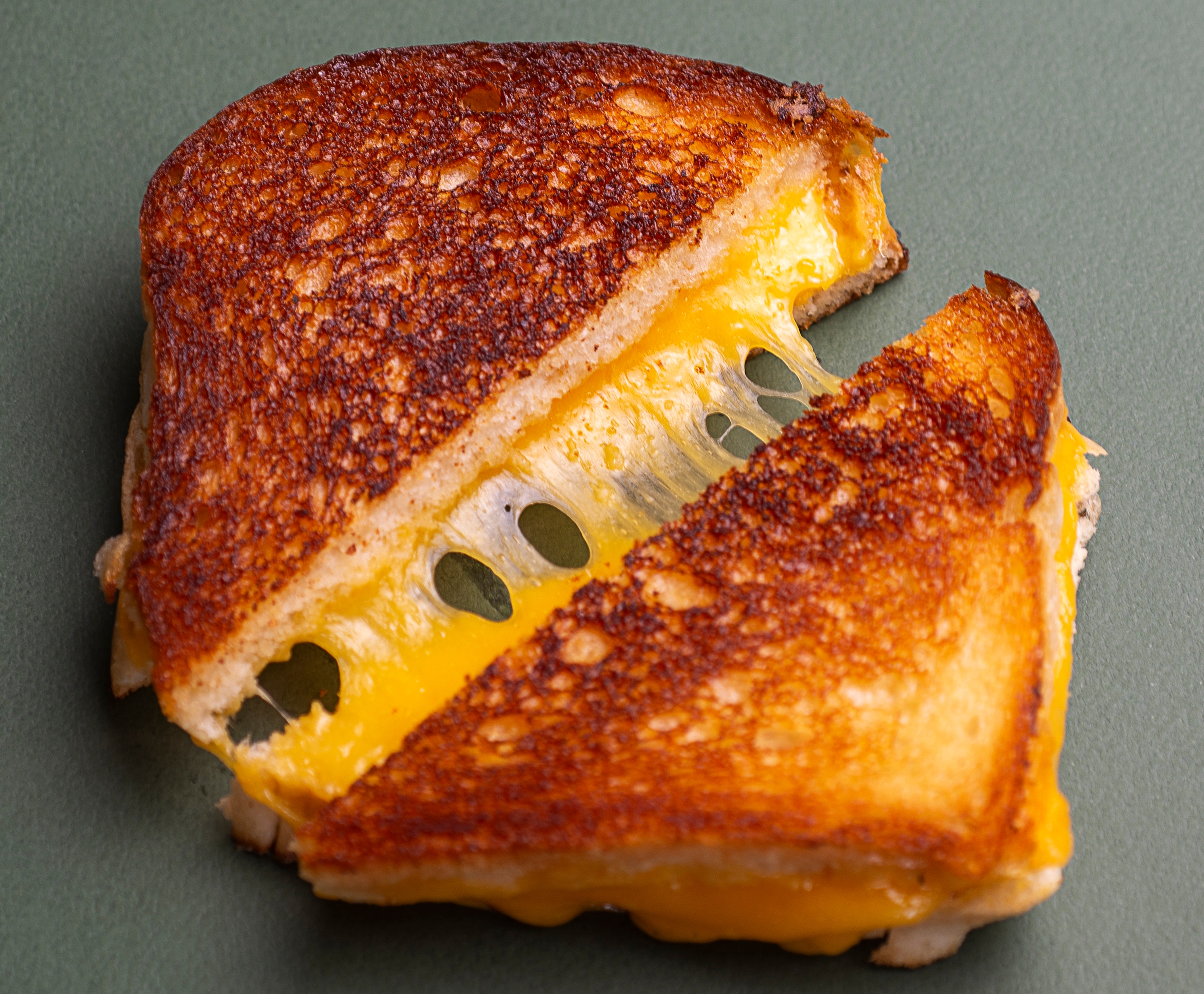 Grilled cheese sandwich with melted cheese oozing from between two slices of toasted bread, placed on a plain surface