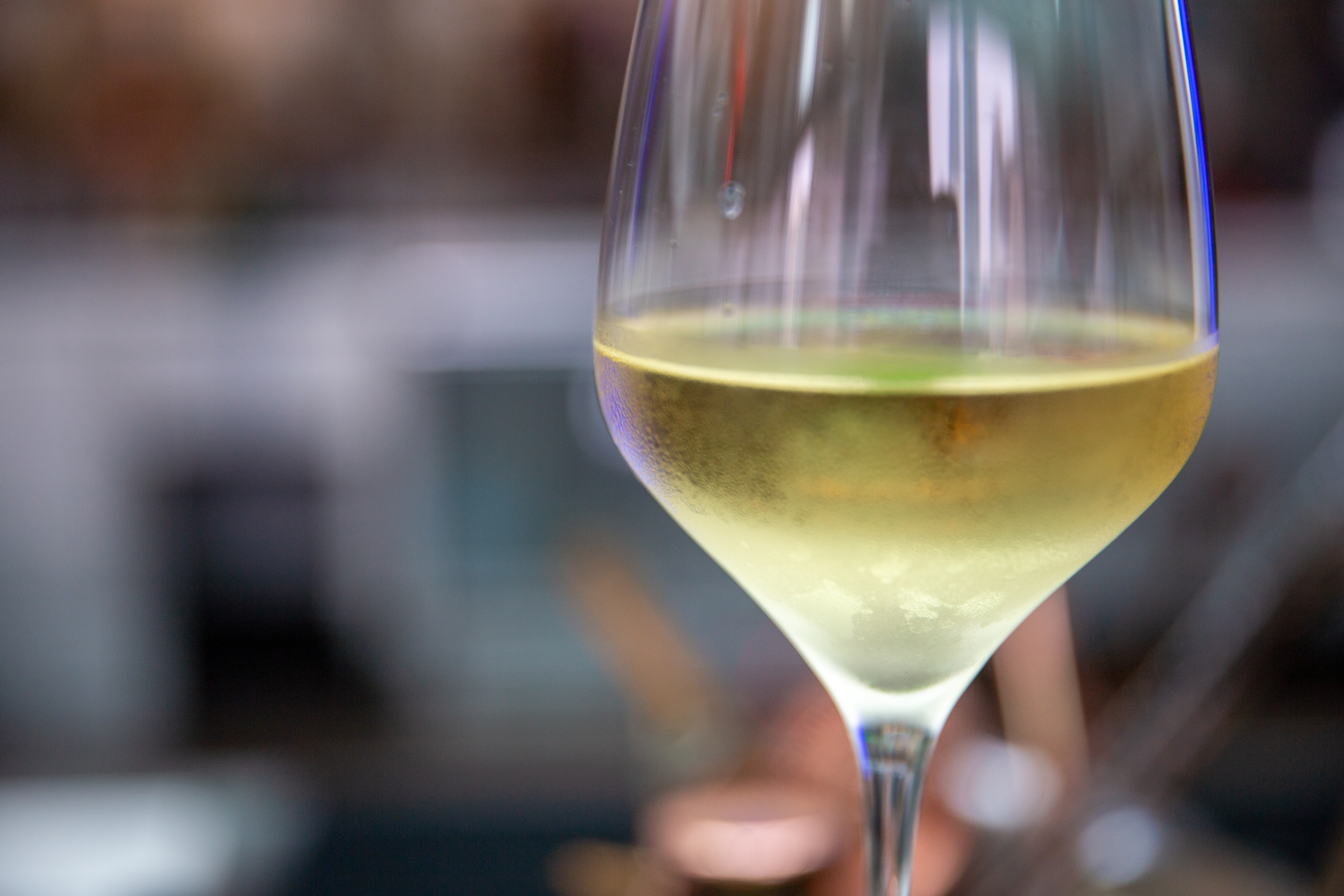 A close-up of a wine glass filled with white wine, with a blurred background
