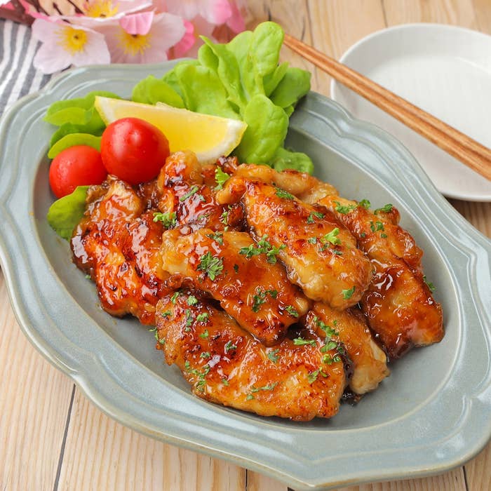 皿に盛られたグレーズのかかったチキンウィング、レモンスライス、レタス、ミニトマト。箸と皿が横に置かれている。