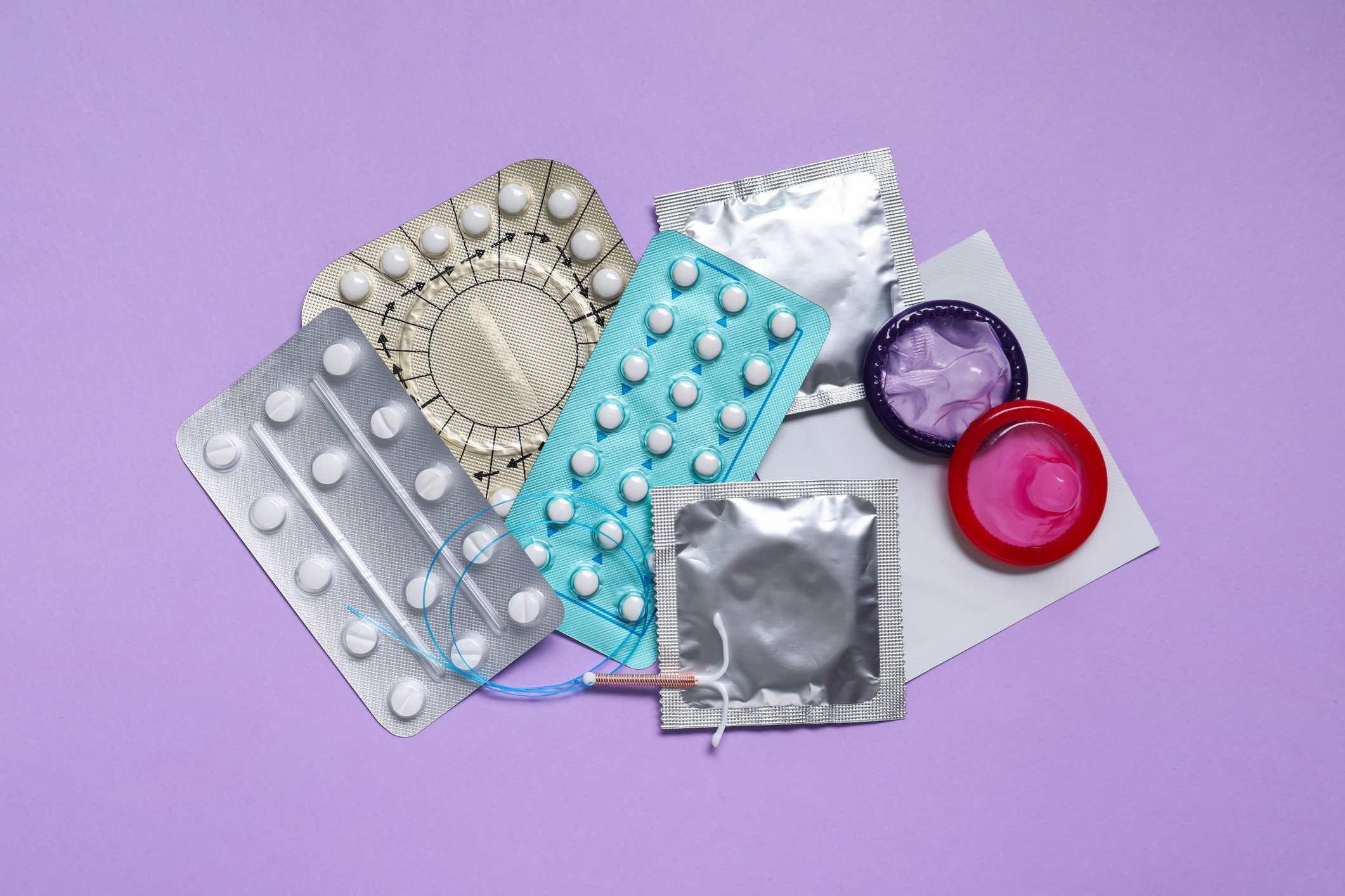 Assorted contraceptives including pill packs, a condom, and a diaphragm displayed against a plain background