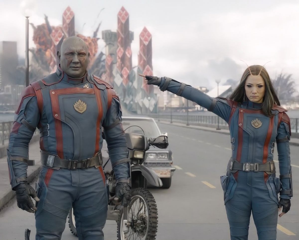 Personajes de ciencia ficción en trajes espaciales, uno señalando hacia adelante, con un fondo urbano futurista