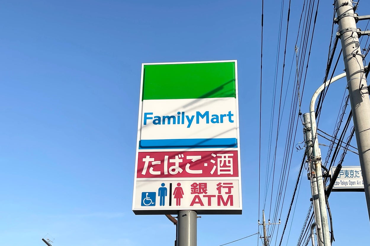 青空の下、ファミリーマートの看板があり、たばこ、酒、ATM、車椅子対応のサービスが表示されています。
