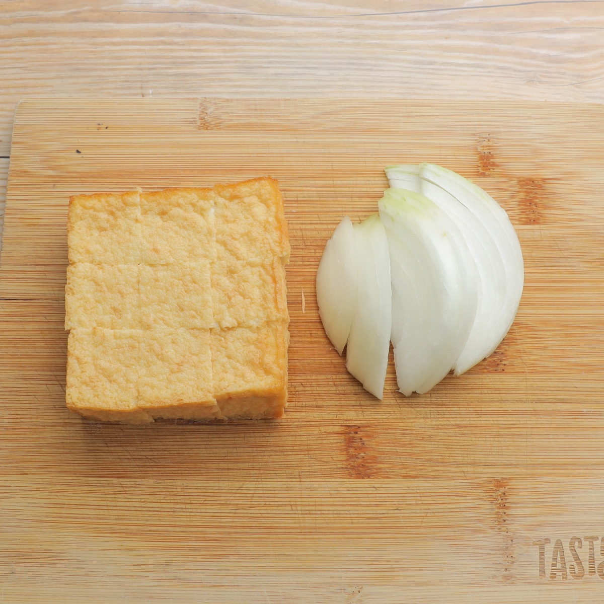 木のまな板の上に豆腐の揚げ物と薄切りの玉ねぎが並んでいる。