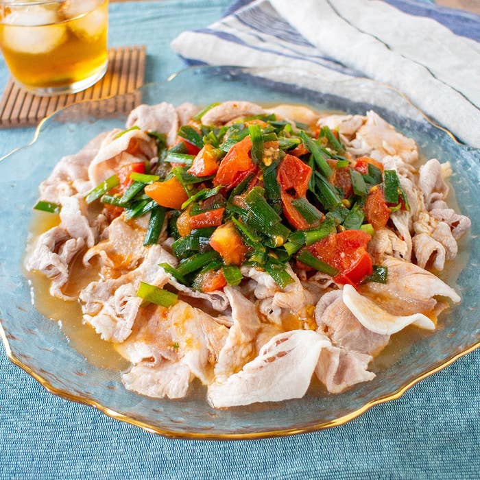 皿に盛られた冷しゃぶサラダ。湯通しされた薄切り肉にトマトとネギが載っている。飲み物とナプキンも見える。