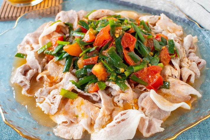 ガラス皿に盛られた薄切り豚肉の上に、トマトやネギが載った料理。横に冷たいドリンク。