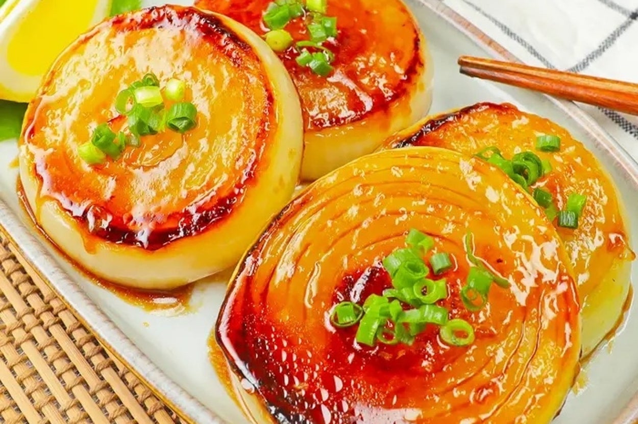 照り焼き風オニオンステーキが皿に盛られ、ねぎがトッピングされている。横には箸とレモンのくし切りが添えられている。