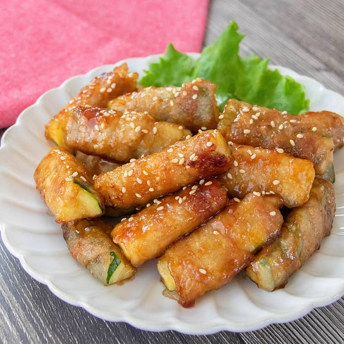 お皿に盛られた肉巻きズッキーニ。白いりごまがトッピングされ、美味しそうに焼き上がっている。バックにレタスが添えられている。