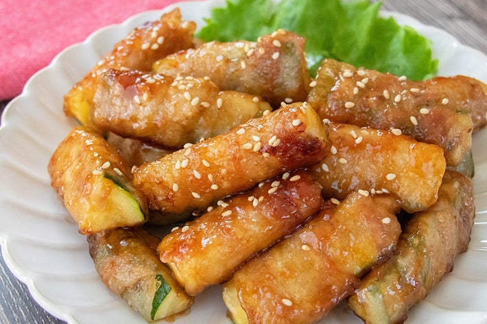 お皿に盛られた肉巻きズッキーニ。白いりごまがトッピングされ、美味しそうに焼き上がっている。バックにレタスが添えられている。